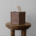 Brown leather tissue box on a wooden stool with a plain background