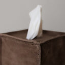White tissue peeking out from a brown tissue box cover against a neutral background