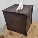 Brown leather-covered tissue box on a wooden surface with a white tissue peeking out.
