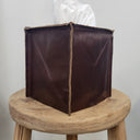 Brown leather tissue box cover on a wooden stool against a plain background
