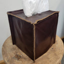 Brown leather tissue box on a wooden surface with a white tissue inside.