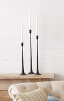 Three black candlesticks with white candles on a wooden surface against a white wall.
