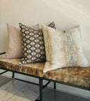 Three decorative throw pillows displayed on a bench with a brown faux-fur cushion, set against a plain off-white wall.