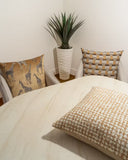 A styled interior corner showing two decorative throw pillows on cream-colored armchairs beside a light marble dining table. One pillow features a giraffe pattern on a tan background, and the other features a woven tan and cream houndstooth pattern.