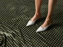 White pointed-toe shoes on a textured green surface