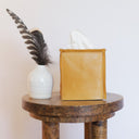 yellow leather tissue box cover on a wooden table with a white vase and feather