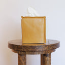 Yellow leather tissue box cover on a wooden table with a white background