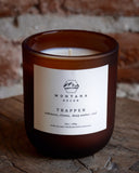 Montana Decor candle labeled 'Trapper' on a rustic wooden surface with a brick wall background.