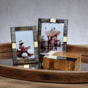 Two decorative picture frames with textured dark wood and gold-toned metal accents, holding printed photos, styled on a wooden tray next to a wooden box against a gray wall.