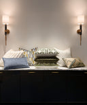 Decorative pillows on a dark surface with wall sconces in the background.