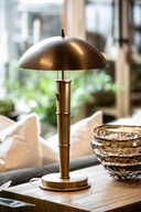 Antique inspired brass table lamp with domed shade and bamboo-style stem, styled on a side table with a textured glass bowl in a cozy living room setting.