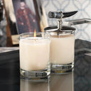Two candles in glass holders with a metallic lid on a reflective surface.