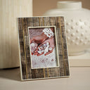 A rectangular photo frame with a vertical bone pattern in brown and beige, standing on a light surface. The center shows a sample photo insert of hands holding white flowers, with a softly blurred cream-colored ceramic vase in the background.