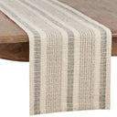 A woven table runner with vertical stripes in beige and gray, draped over a wooden table against a white background.
