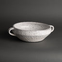 Speckled white ceramic bowl with handles on a dark background