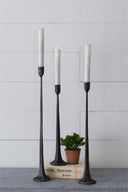 Three black candle holders with white candles on a light gray surface and background.