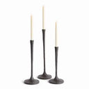 Set of three slender black metal taper candle holders in varying heights with round bases and ivory candle and white background