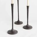 Close up shot of three slender black metal taper candle holders in varying heights with round bases and ivory candle and white background 
