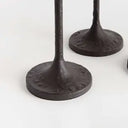 Close-up of a dark cast iron candle holder base with a textured circular foot and a vertical stem, shown on a plain light background with another similar base partially visible behind it.