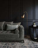 Gray sofa with decorative pillows in a room with dark paneled walls and a gold floor lamp.
