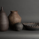 Four dark brown ceramic vases on a gray background