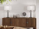 A mid-century modern wooden credenza or sideboard cabinet with two black metal table lamps and decorative objects on top, set against a textured light gray wall.