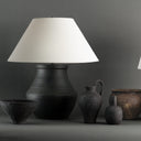 Decorative lamp with a white shade and dark ceramic base, surrounded by other ceramic items on a gray background.