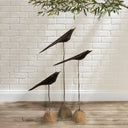 Set of three black wood and metal bird sculptures on slender stands with natural stone bases with white background