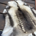 A natural animal fur pelt with a gray, black, and cream spotted pattern, laid flat on dark brown wooden decking.