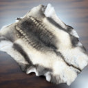 A natural animal fur pelt rug with a gray, black, and cream fur pattern, laid flat on a dark wood surface.
