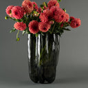 A bouquet of pink and coral dahlia flowers with green stems arranged in a glossy black ribbed vase against a smooth gray studio background.