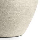 Close-up of a textured ceramic vase in a light warm gray-beige tone, showing the rough stoneware surface and a small dark base edge against a white background.