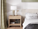 Bedroom with wooden nightstand, lamp, and books next to a bed with white bedding.