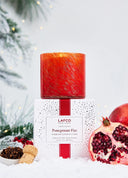 LAFCO Pomegranate Fizz scented candle in a vibrant red glass vessel with subtle gold marbling.  Sitting on top of the white, red confetti box with pomegranates and cloves on the side  