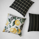 Three decorative pillows on a white surface, including a black plaid pillow the Bond-Onyx Pillow 24x24, a lemon-patterned pillow, and a black striped pillow.