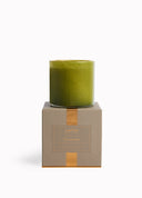 A green glass jar candle displayed on top of its textured taupe packaging box with a gold ribbon, against a clean white background.