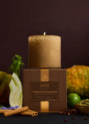 A lit LaFco New York candle in a textured metallic gold cylinder sits atop its brown box, surrounded by autumnal ingredients like cinnamon sticks, star anise, a lime, and sliced onion against a dark brown background.
