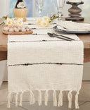 Cream woven table runner with thin black stripes and tasseled fringe, styled on a rustic wood table