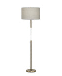 A modern floor lamp with a cylindrical light beige fabric drum shade, a brushed brass metal stand, and a clear glass cylindrical accent in the center, set against a plain white background.