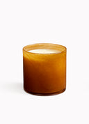 An amber glass jar candle with white wax, photographed against a clean white background.