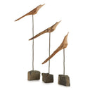 Set of three natural wood and metal bird sculptures on slender stands with natural stone bases with white background