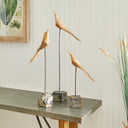Set of three black wood and metal bird sculptures on slender stands with natural stone bases with white background