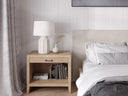 Bedroom with wooden nightstand, lamp, and books next to a bed with gray bedding.