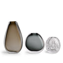 Three modern glass vases in graduated sizes on a white background. The left vase is smoky brown, the middle is smoky gray, and the right is clear glass with a raised bubble pattern.